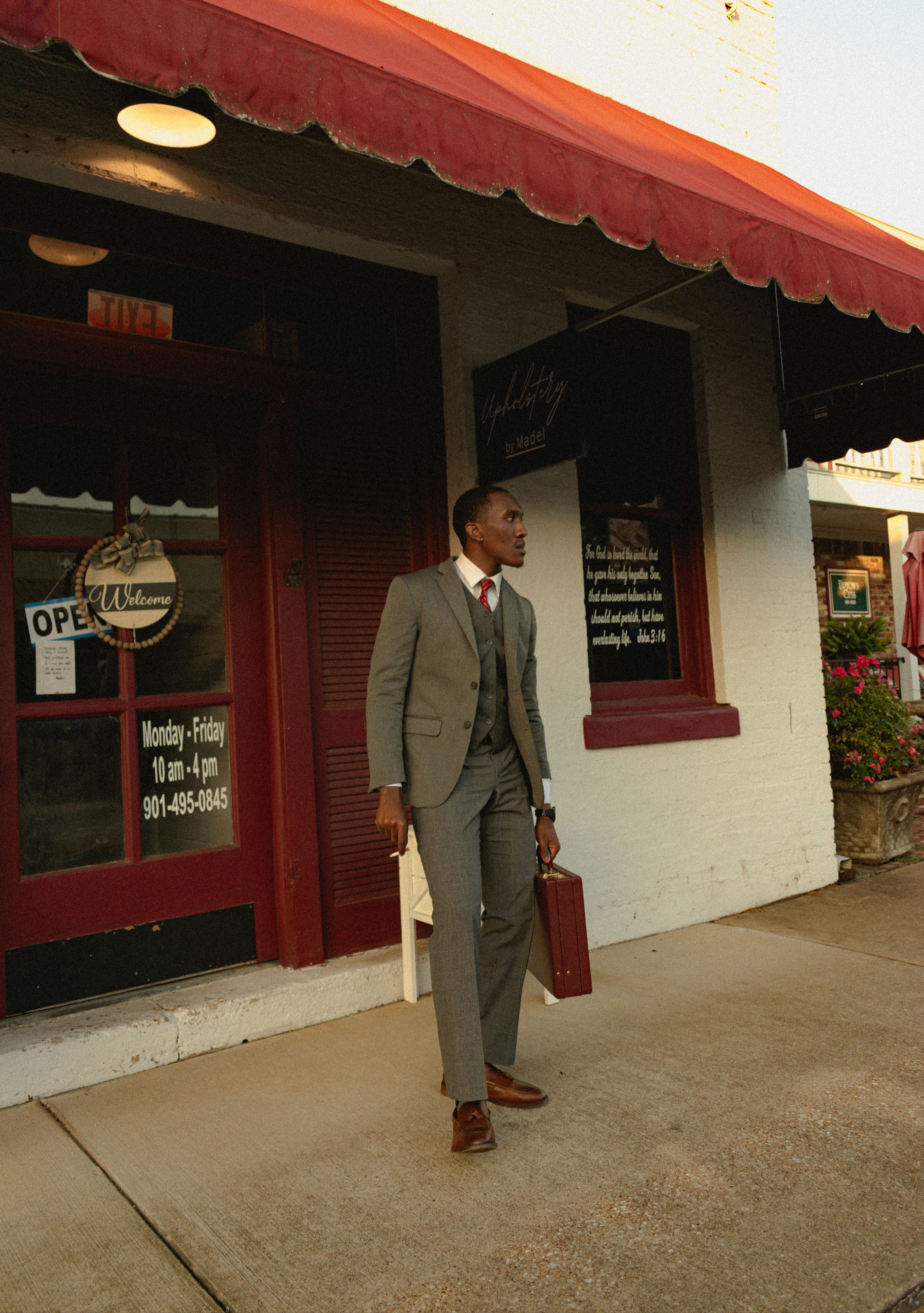 Man in a suit walking outside a building with a red awning